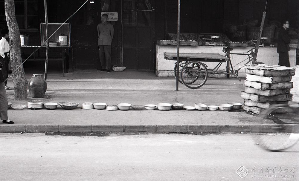 北京和平里副食店门口排队买豆腐，每人限买两块，人们让盆碗排队，自己晨练去了。排队的盆成为人物活动的延伸。1981年.jpg